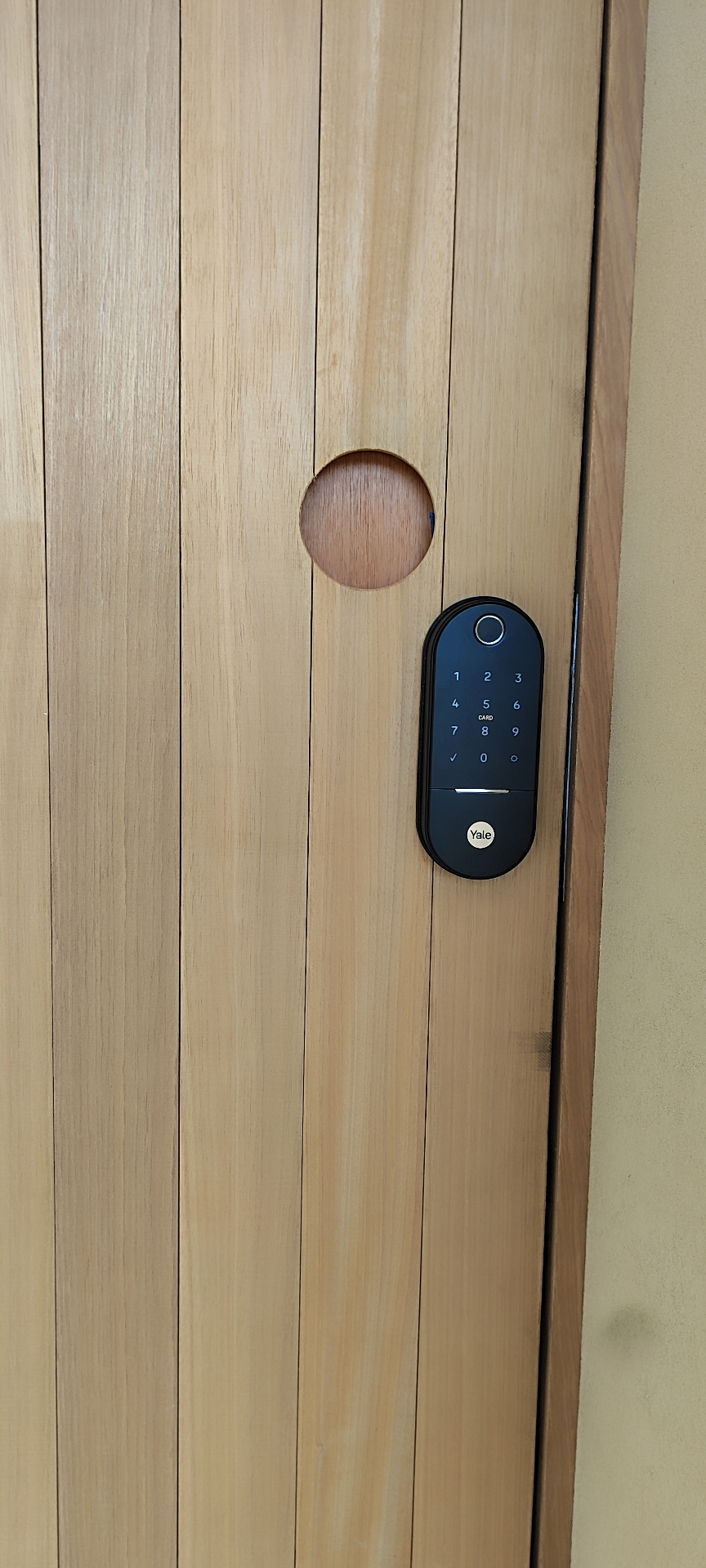 Yale compacta com biometria em porta de madeira clara